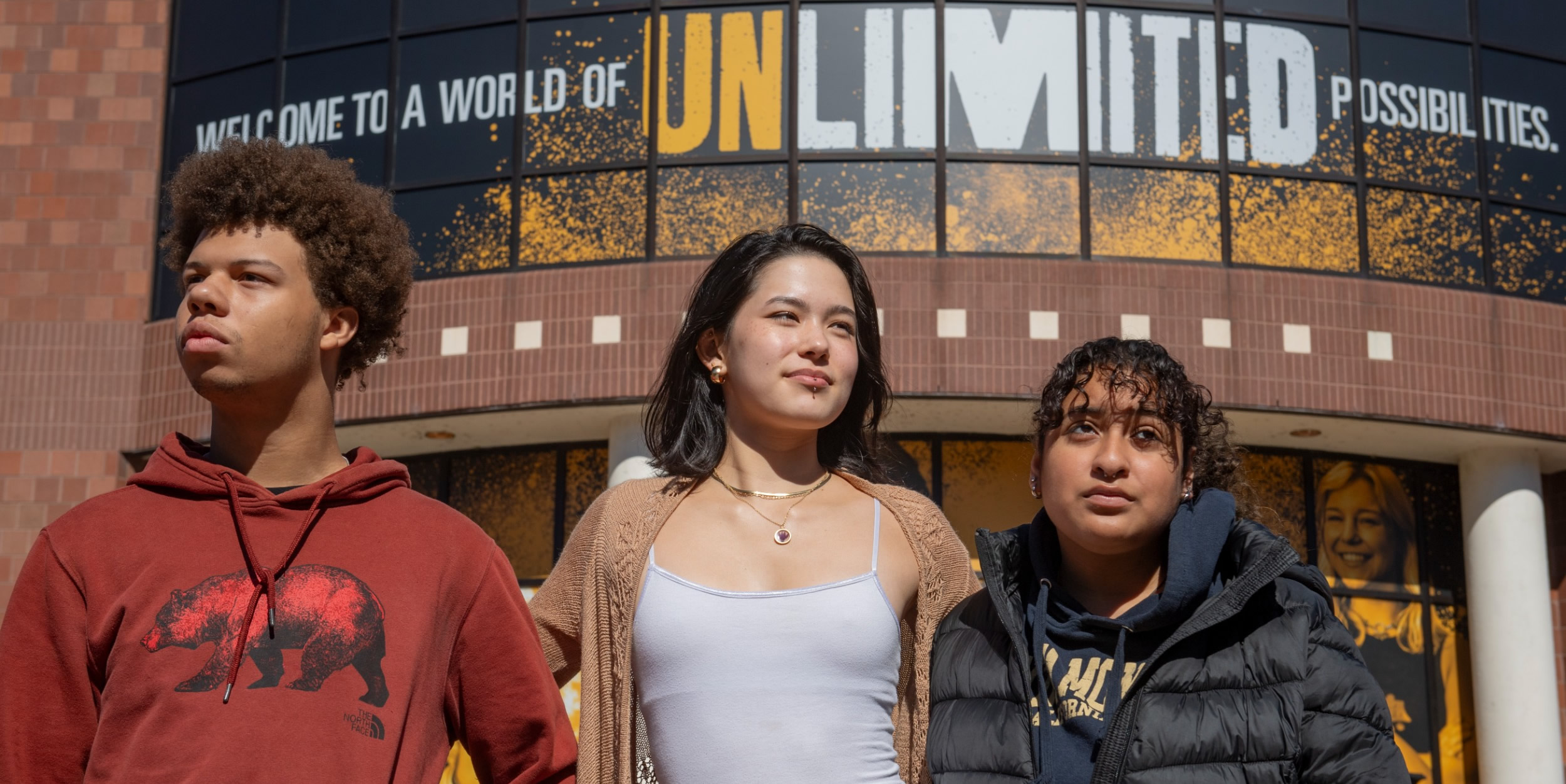 image shows 3 students in frnt of unlimited sign